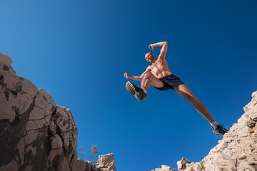 Active fast running mountain sky runner smiling and jumping over the cleft cliff during the high...