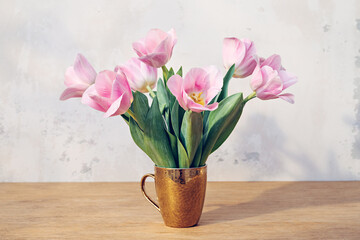 Pink tulips in a golden cup on a wooden table