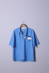 Doctor shirt with stethoscope, badge and pen hanging on light grey background