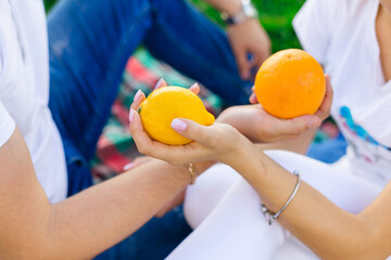 Naklejka premium close up of the hands of young people exchanging delicious oranges while sitting on blankets in nature.
