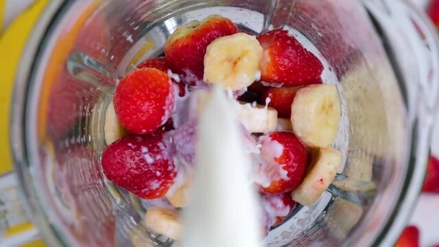 Cooking strawberry and banana milkshake or smoothie with milk poured into blender. top view. slow motion. Healthy drink concept
