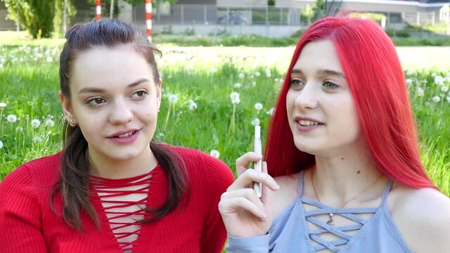 Two beautiful Girls smoking Iqos electronic Cigarette in Summer Park