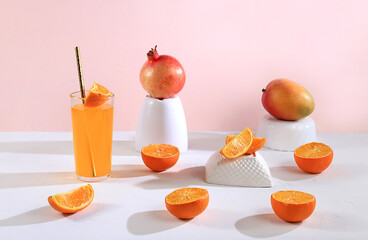 Modern still life with citrus, orange juice and oranges, pomegranate and mango on stand and podiums...