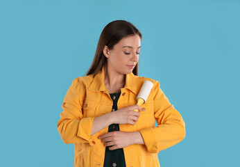 Young woman cleaning clothes with lint roller on light blue background