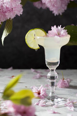cocktail margarita with a slice of lime on the background of a bouquet of pink sakura, still life with a refreshing drink