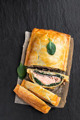 Homemade salmon wellington with spinach and mushrooms on rustic wooden table