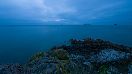 Fototapeta na wymiar Rochers en mer en pose longue de nuit sous un ciel gris