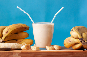 Vista de un batido de leche con plátanos y rodajas de plátanos rodeando el vaso.