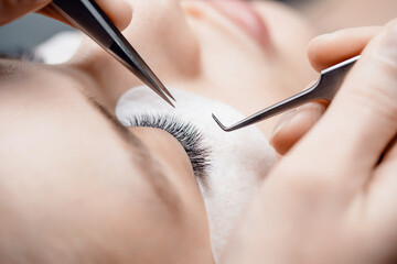 Eyelash extension procedure. Master tweezers black fake long lashes beautiful female eyes