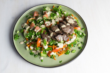 salad with fried beef, vegetables, sauce on green plate on white background