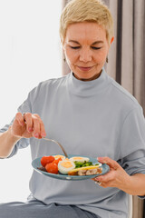 Mature women have breakfast with healthy food on a plate. Fresh bio vegetables and eggs. Healthy nutrition concept