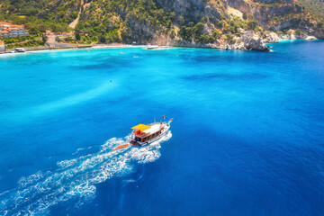 Fototapeta na wymiar Speed boat in blue sea at sunrise in summer. Aerial view of floating motorboat in sea bay. Tropical landscape with yacht, clear water, rocks , stones, mountain, green trees. Top view. Oludeniz, Turkey