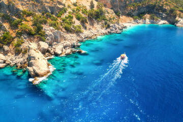 Speed boat in blue sea at sunrise in summer. Aerial view of floating motorboat in sea bay. Tropical landscape with yacht, clear water, rocks , stones, mountain, green trees. Top view. Oludeniz, Turkey