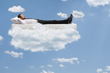 Businessman lying on a mattress with clothes and shoes in the clouds