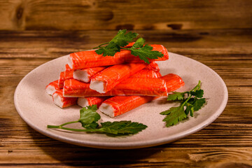 Ceramic plate with pile of crab sticks and parsley twig on a wooden table