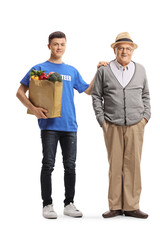 Young male volunteer holding a grocery bag and standing next to elderly man