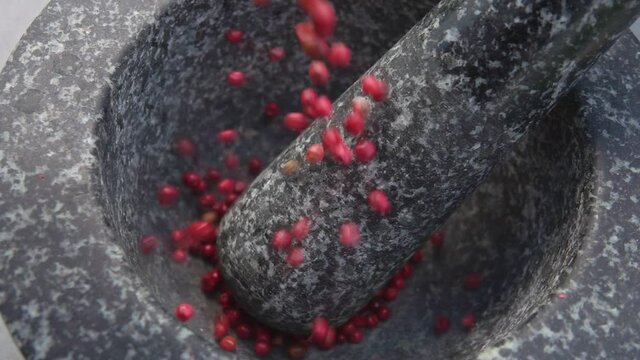 Close-up of spicy rose peppercorns falling and bouncing in a grey stone mortar
