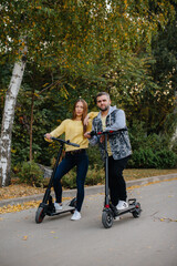 A young beautiful couple rides electric scooters in the Park on a warm autumn day. Hobbies and recreation.