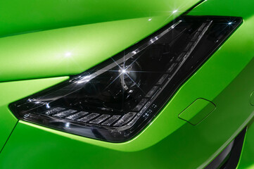 Headlight of sports car with sparkling stars, hood, fender and bumper details of sedan with green bodywork, automobile industry 