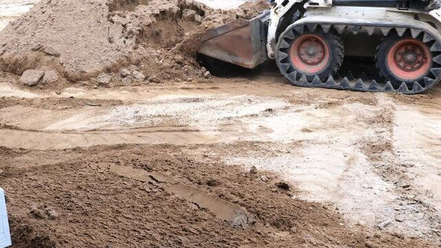 Closeup clip of a compact front loader as it lifts and spreads a load of dirt at a construction job site.