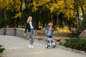 A mother teaches her little daughter to ride a Segway in the Park during sunset. Happy family vacation.