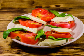 Fototapeta na wymiar Plate with caprese salad (italian salad with cherry tomatoes, mozzarella cheese and basil leaves) on wooden table