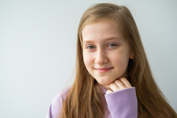 portrait of beautiful teenage girl with long hair in purple hoodie standing against white wall