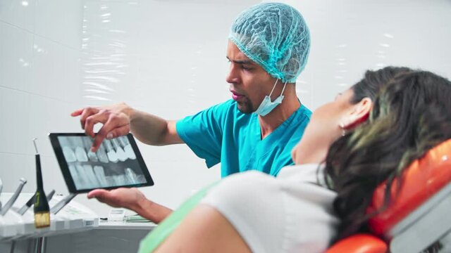Doctor in the dental office with patient at the examination, doctor showing the roentgen image on a tablet