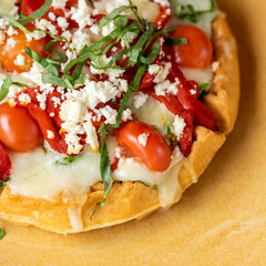 Delicious golden waffle with melted cheese, cherry tomato, roasted bell peppers, and feta cheese.
