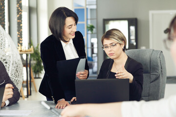 Two young business women in the office, analyzing information looking into a laptop and smiling