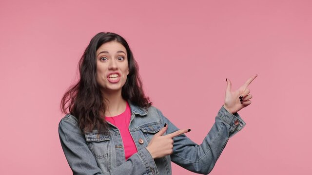 Shocked woman 20s years old in casual denim jacket pink t-shirt posing look camera pointing fingers hands on copy space workspace isolated on pink background. People lifestyle concept. Excited girl.