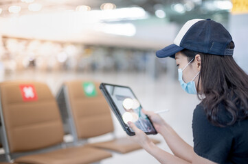 Female wearing surgical mask and hand holding the gadget while waiting boarding time at the airport, Due to the Covid 19 epidemic pandemic.