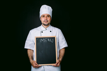 Chef cook with jacket and kitchen hat, holding a piazarra with the menu, on black background