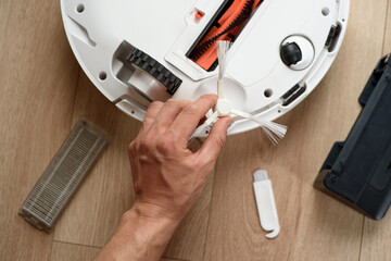 A man pulls out a brush of a robot vacuum cleaner for cleaning