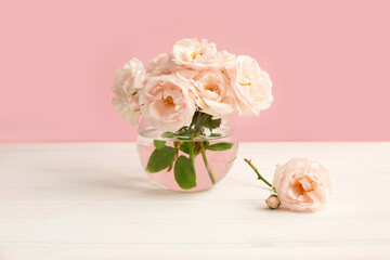 Tender light garden roses in a transparent vase on pink pastel background.