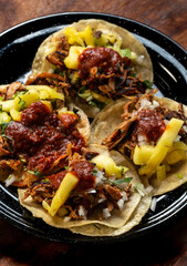 Tacos al pastor con piña y salsa mexicana, cebolla y cilantro en un plato negro de peltre