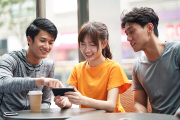 three young asian adults looking at cellphone