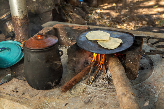 Tortillas en comal de fuego de le&ntilde;a junto a olla de barro con frijoles