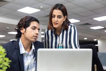 Portrait of two young serious businesspeople looking at laptop and discussing project at...