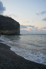 The sunrise over the calm sea casts rays of orange light into the air as the setting sun penetrates through the clouds into the picturesque calm seascape