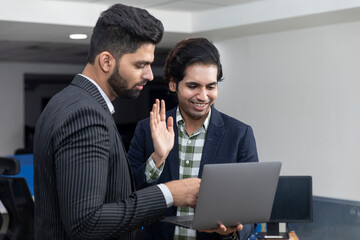 Fototapeta premium Portrait of two young handsome Indian businessmen looking into phone, discussing project, corporate environment.