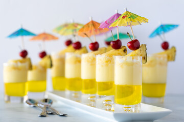 Several pineapple layered parfaits garnished with pineapple wedges, cherries and mini umbrella picks.