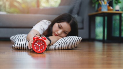 Young asian woman reaching over to turning off alarm clock while lying on the floor in living room...