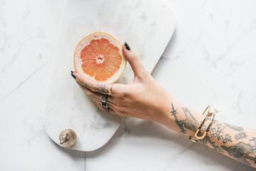 Tattooed woman holding an orange over a marble background