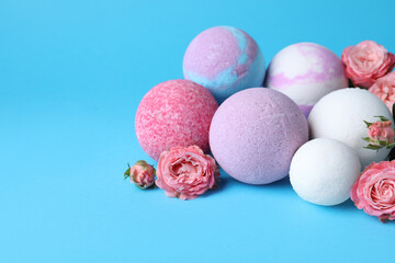 Colorful bath bombs and beautiful roses on light blue background, space for text