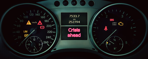 CRISIS AHEAD is written on the dashboard of the car next to the controls and mileage indicators.