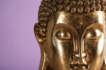 Beautiful golden Buddha sculpture on violet background, closeup. Space for text
