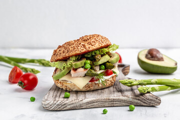 Healthy burger with chicken fillet, asparagus, avocado, tomatoes, peas, cheese and tartar sauce on rustic wooden background. fast food and junk food concept