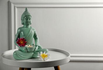 Buddha statue with burning candle and lotus flowers on white table. Space for text