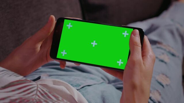 Close up. Chromakey Mockup. Woman at home relaxing reading on the smartphone with pre-keyed green screen